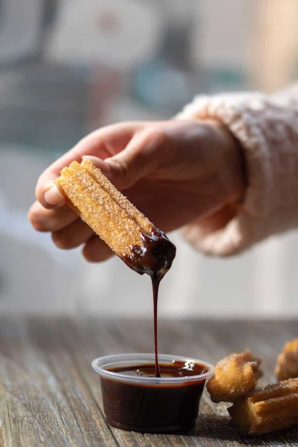 Woman holding churro while chocolate drips
